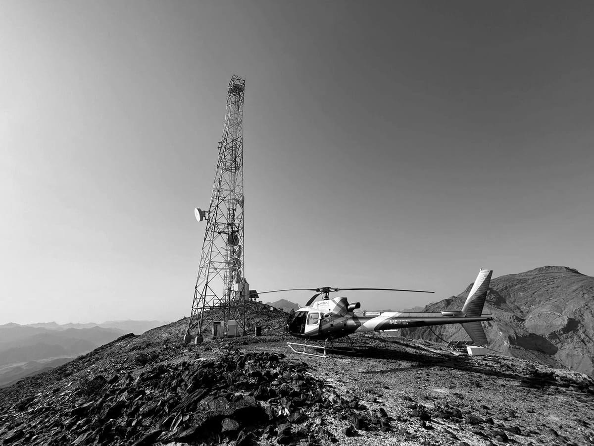 A helicopter parked on a narrow mountain ridge beside a lattice telecommunications tower.
