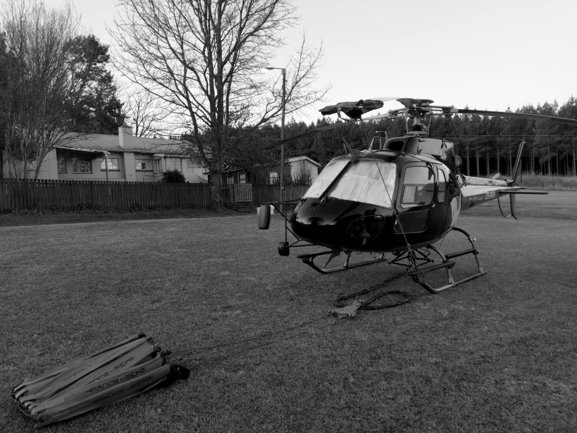A helicopter on grass at first light with a collapsed firefighting water bucket laid out on its line in the foreground.
